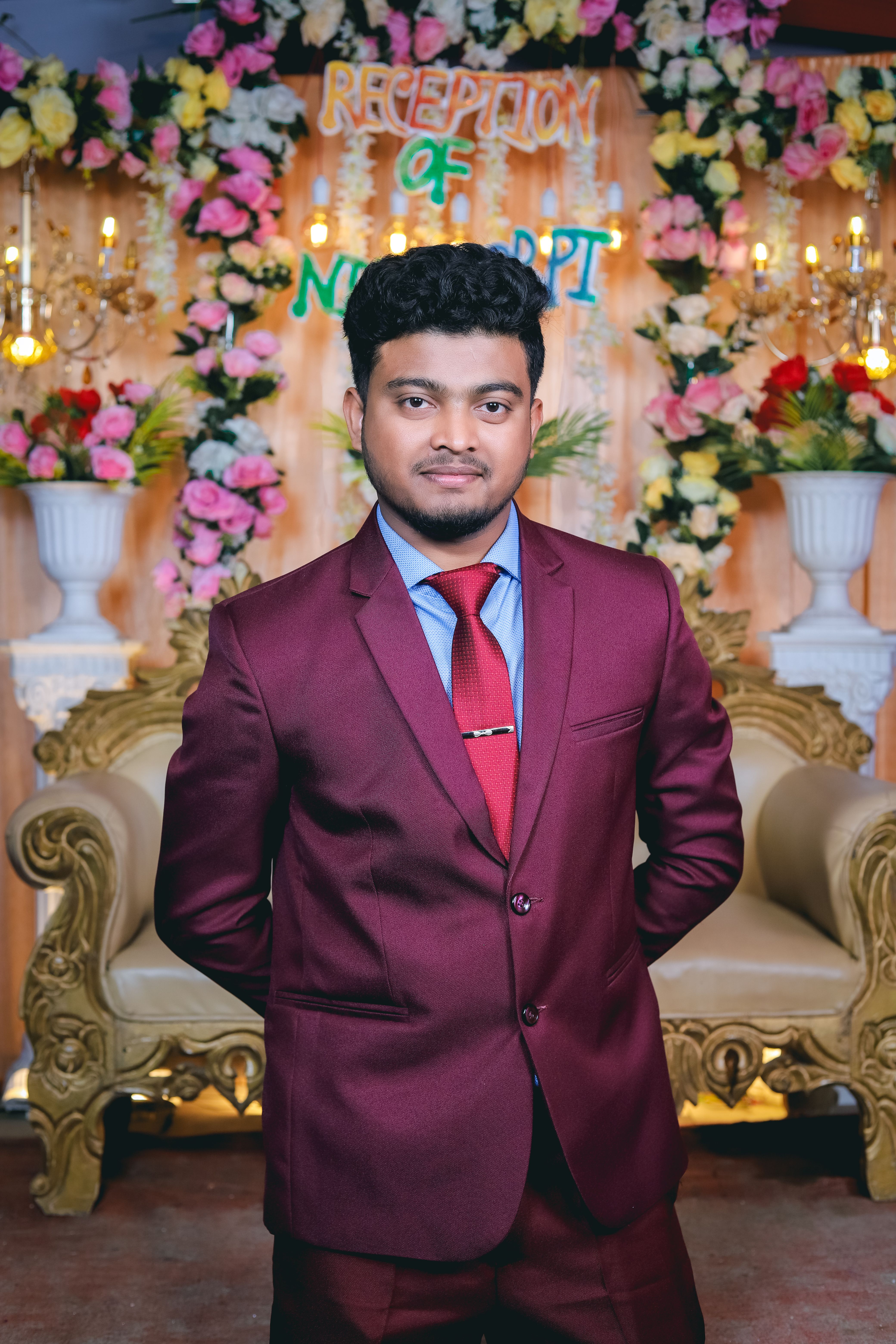 Portrait of a groom in a burgundy suit at a wedding reception with floral decor.
