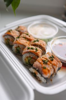 Close-up of sushi rolls garnished with sauces in a takeout box, perfect for Japanese cuisine lovers.