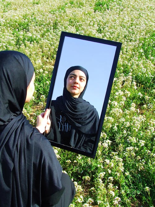 A woman in a black hijab is looking at herself in a mirror