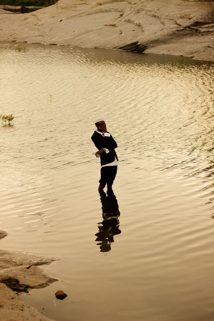 A fashionable man in a suit stands gracefully in a reflective lake at sunset.