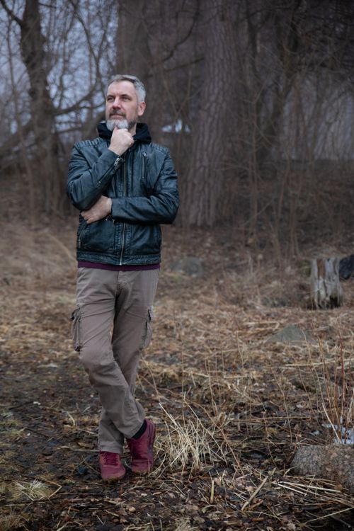 Free A man in a leather jacket standing thoughtfully outdoors in a wooded area. Stock Photo