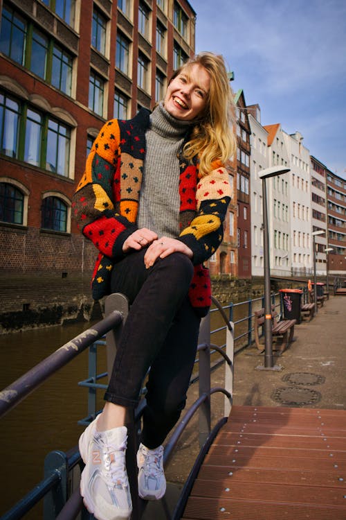Smiling Blonde Woman Sitting on Railing over River in Hamburg