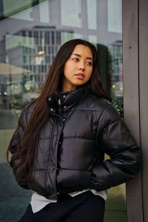 Free Woman in black puffer jacket leaning against a building in Berlin, stylish fashion look. Stock Photo