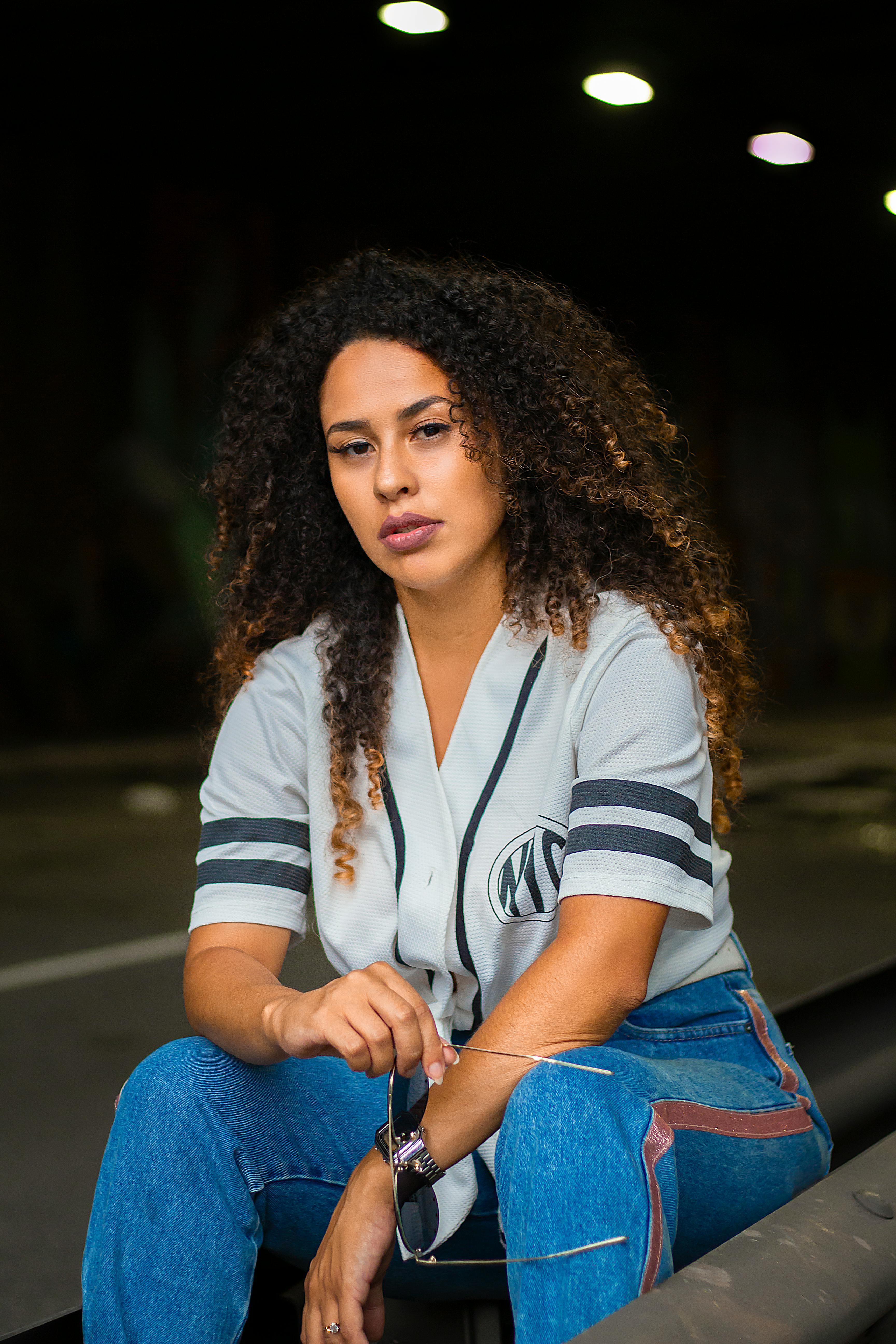 woman in grey shirt and blue jeans sits on side of road