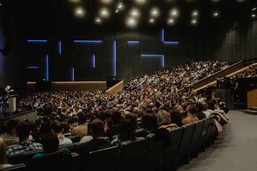 A large audience attentively listens to a speaker at a conference in Oradea, Romania.