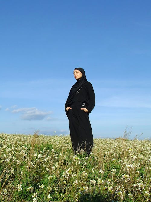 A woman in a black robe stands in a field