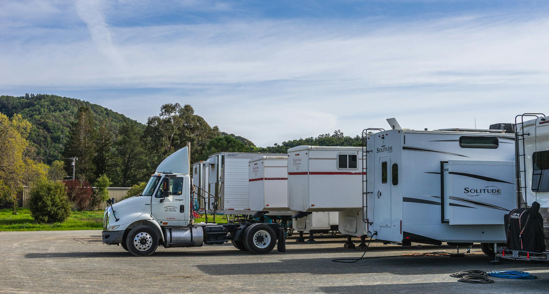 Trucks and RVs parked outdoors with trailers against a scenic mountain backdrop.
