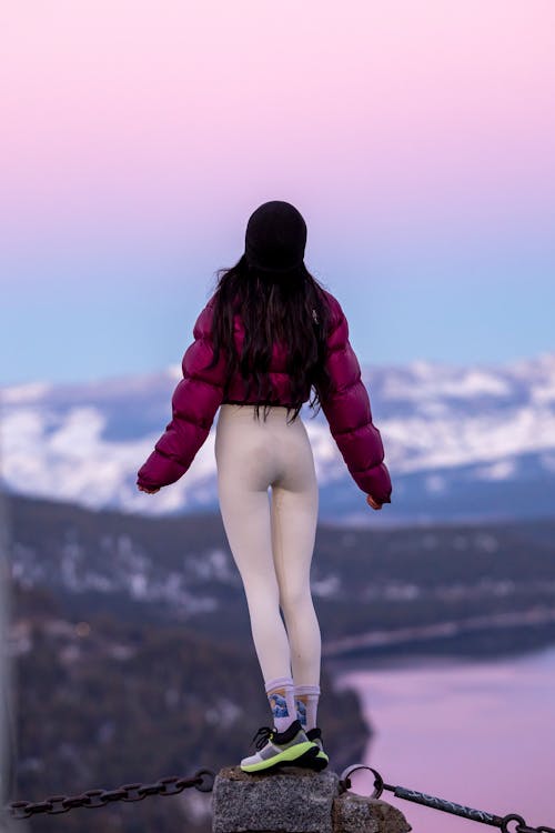 A woman standing on top of a mountain with a pink jacket