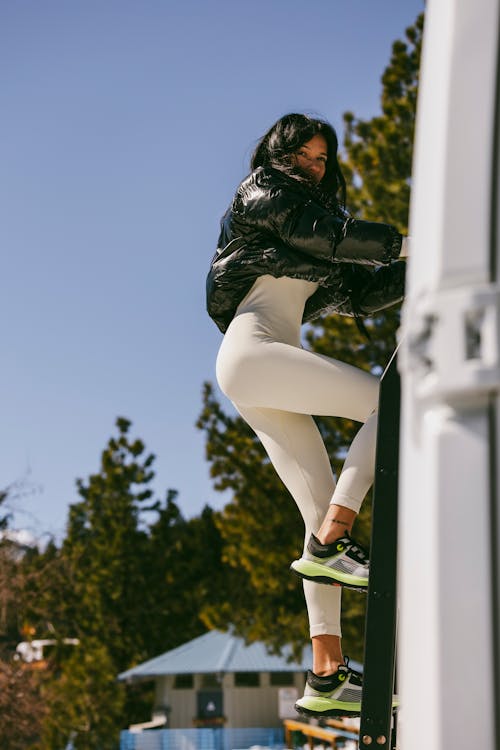 A woman in white leggings and sneakers is leaning against a truck