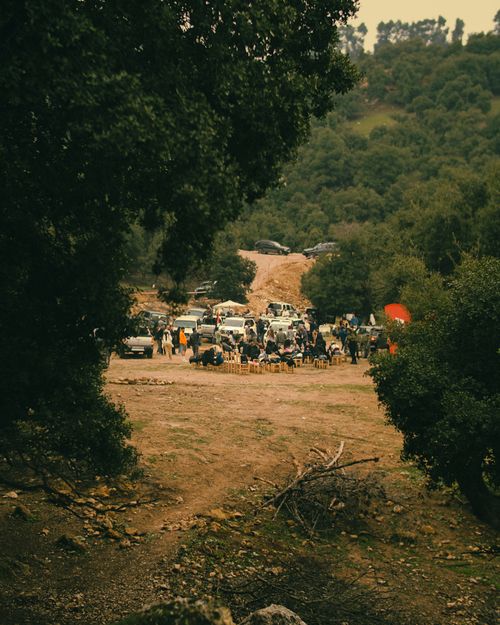 Free A vibrant outdoor gathering with people and vehicles in a lush forest, framed by trees. Stock Photo