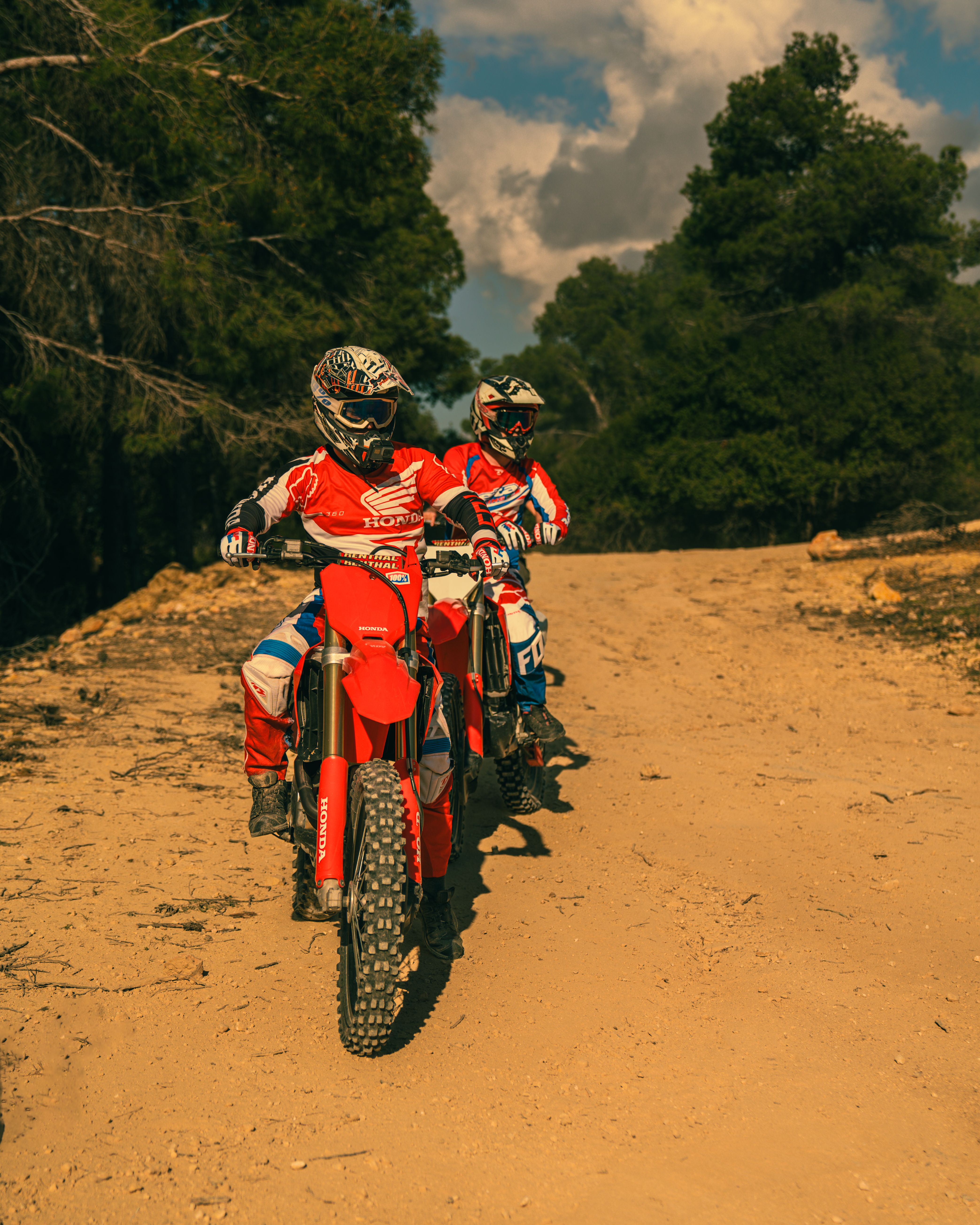 Dynamic motocross riders traverse a rugged dirt trail in the forest, showcasing speed and skill.