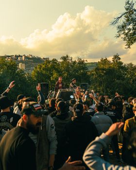 DJ playing live music at an outdoor summer festival with a lively crowd and scenic backdrop.