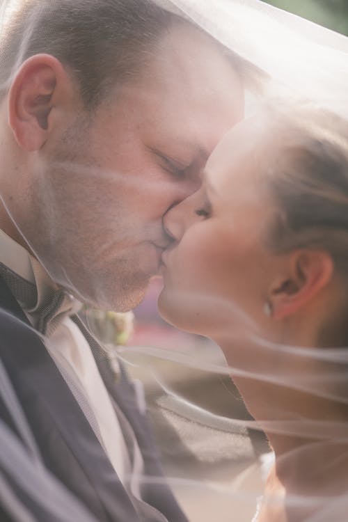 A bride and groom kiss under a veil