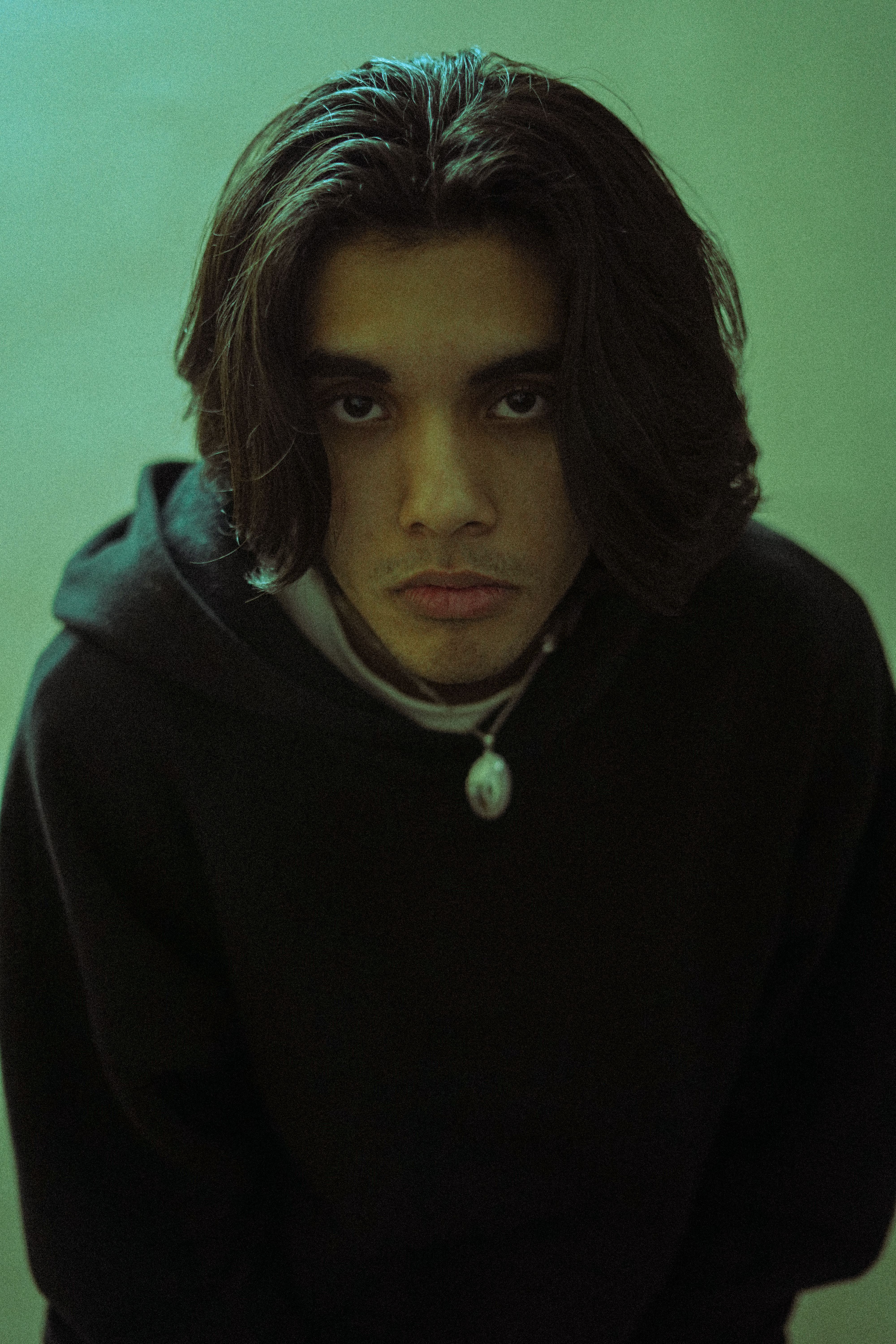 Portrait of a male model with black hair in a fashion studio shoot against a green background.