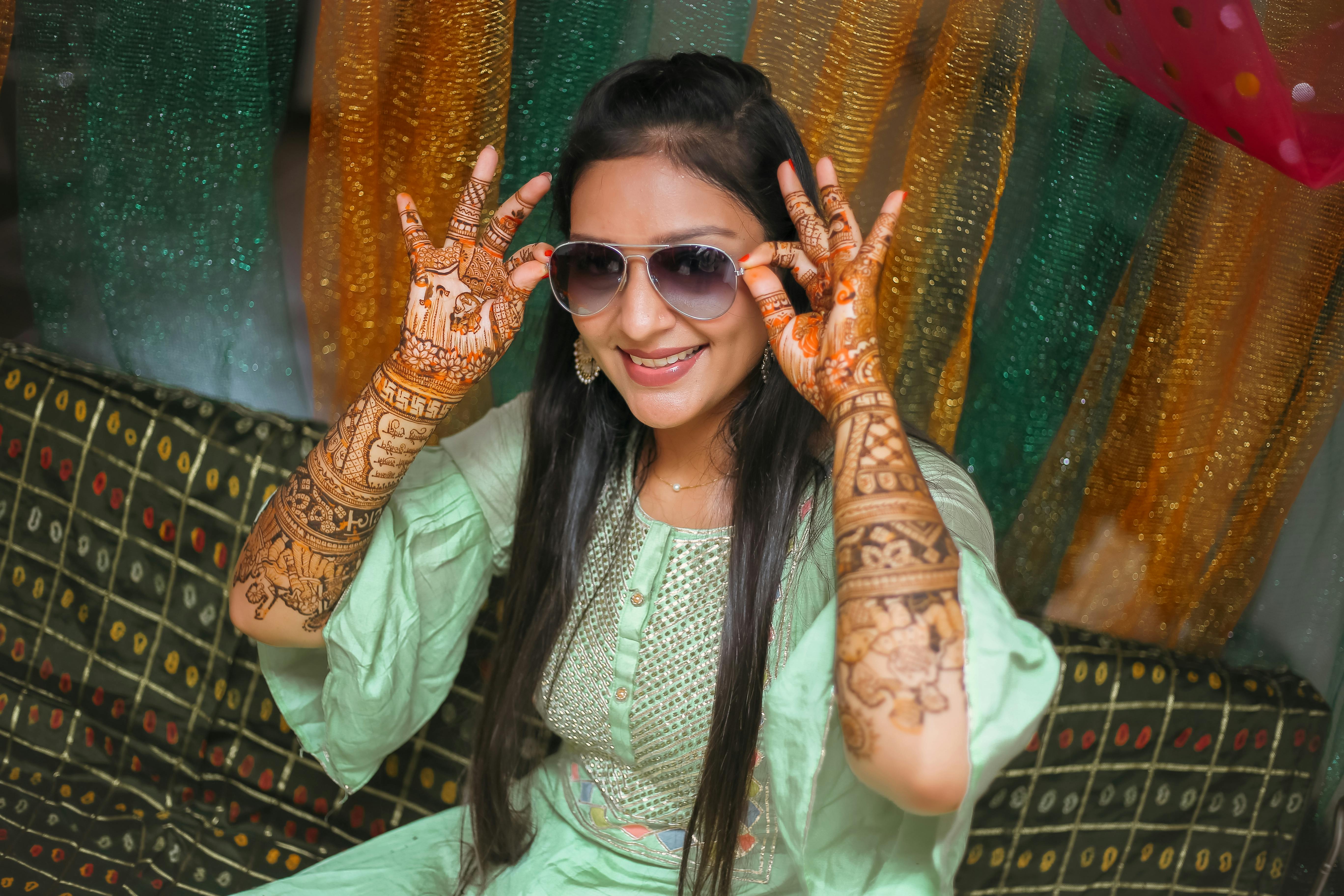 A smiling Indian woman with long hair, glasses, and henna tattoos in traditional clothing at a festive gathering. | Indian Village Development