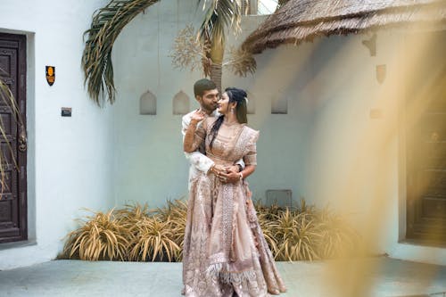 A couple in traditional attire pose for a photo in front of a palm tree