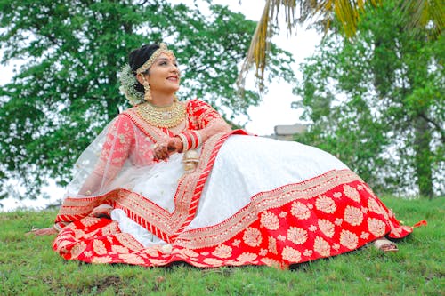 A woman in a red and white lehenga sitting on the grass