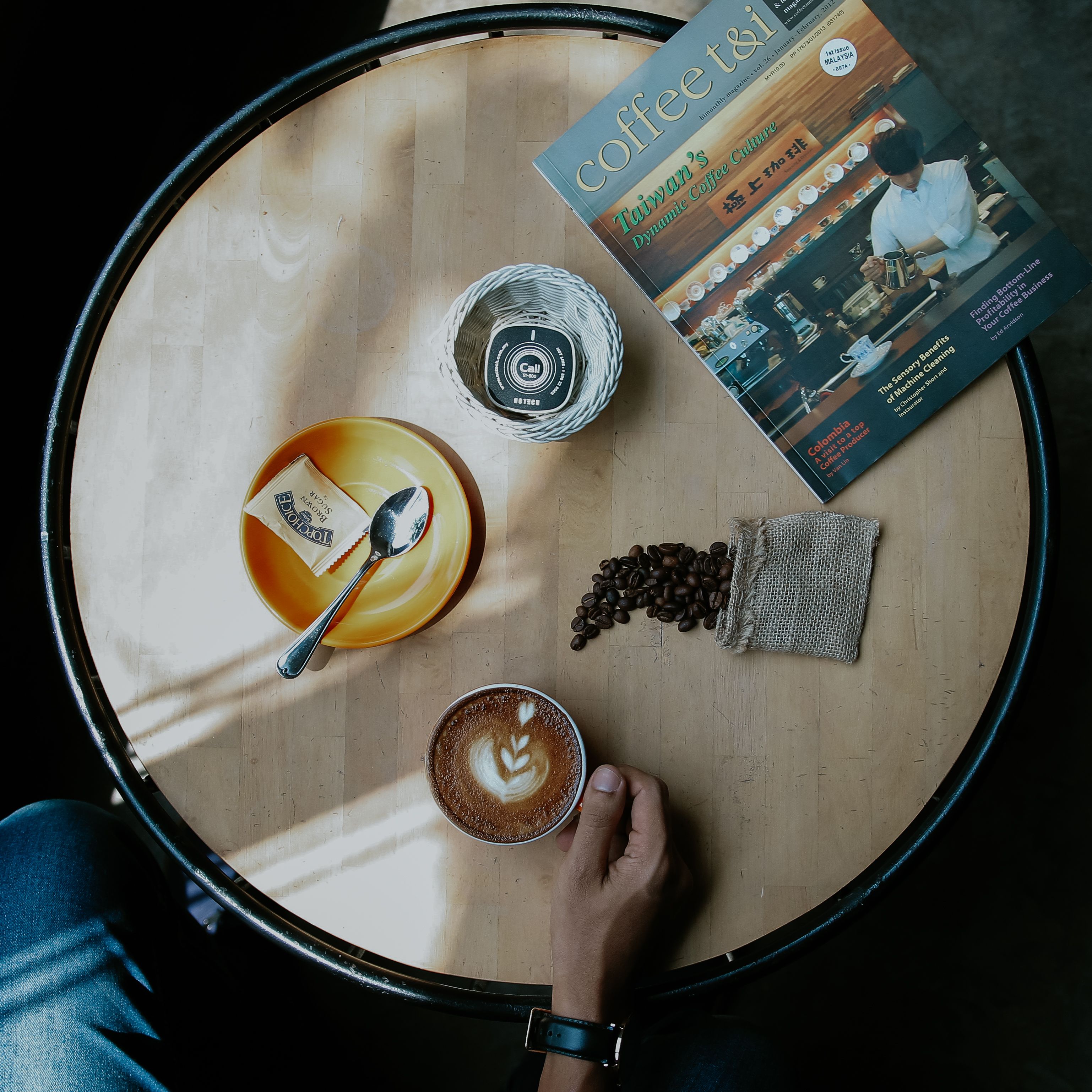 Overhead shot of a coffee table with latte art, coffee beans, and a magazine, capturing the essence of a cozy café atmosphere.
