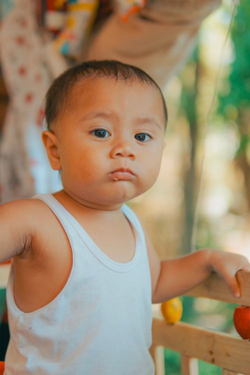 Free Cute toddler in a white tank top standing outdoors with a curious expression, showcasing innocence and playfulness. Stock Photo