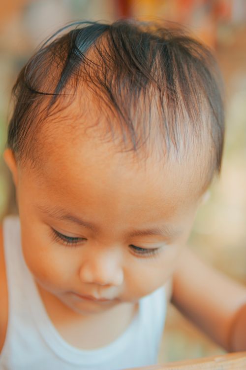 Free Close-up portrait of a baby looking down in soft, natural light, creating a serene mood. Stock Photo