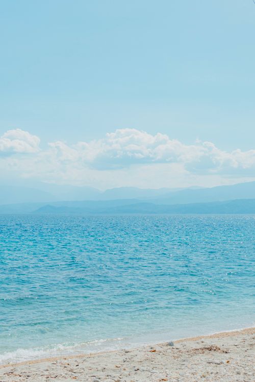 Free Peaceful beach scene with clear blue waters and soft clouds under a bright sky. Stock Photo