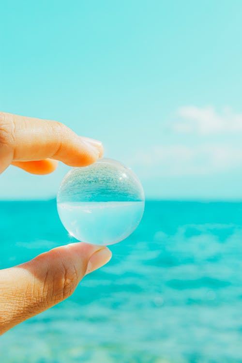 A person holding a clear glass ball in front of the ocean