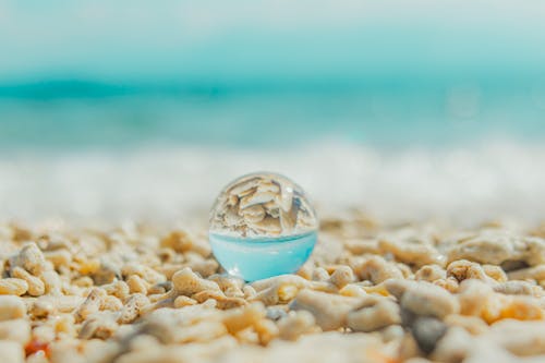 A glass ball sitting on the beach with water in it
