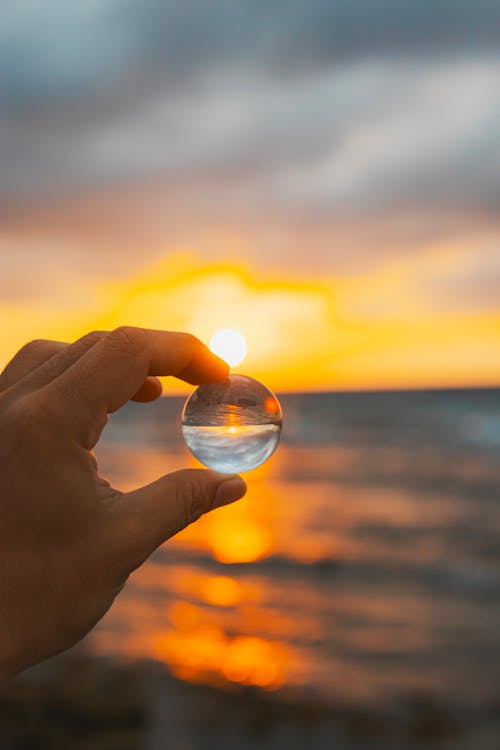 A person holding a glass ball in front of the sunset