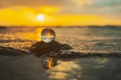 A glass ball sitting on the beach at sunset