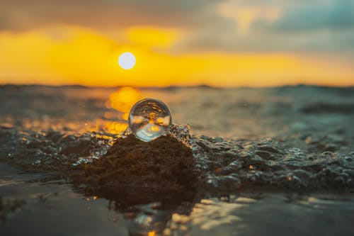 A ball of water on the beach at sunset