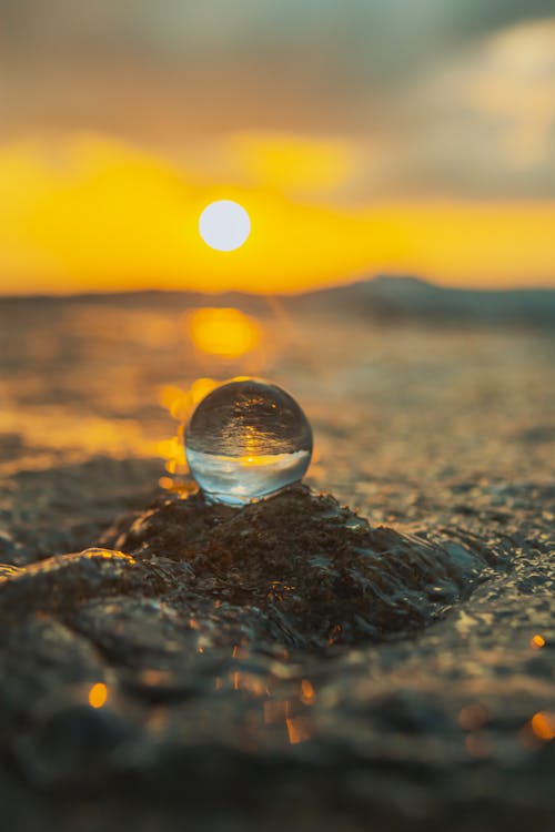 A glass ball sitting on the ground at sunset