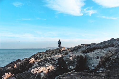 A Person Standing on a Rocky Shore in Distance 