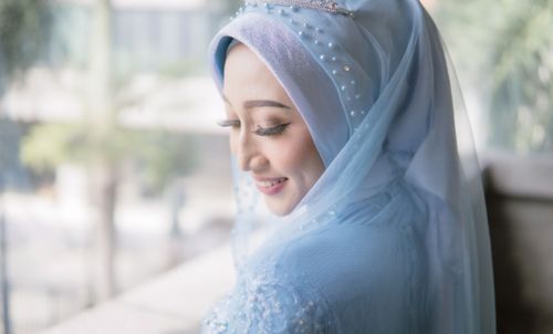Free A beautiful bride in a blue hijab smiles softly, captured in a moment of contemplation indoors. Stock Photo