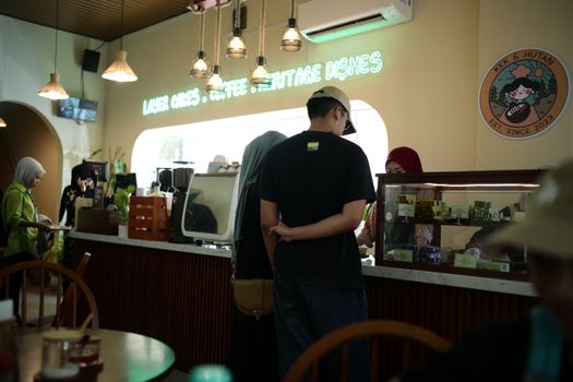 Warm interior of a bustling coffee shop in Kota Bharu with customers and staff interaction.