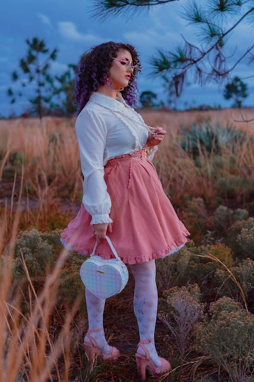 A woman in a pink skirt and white shirt standing in a field