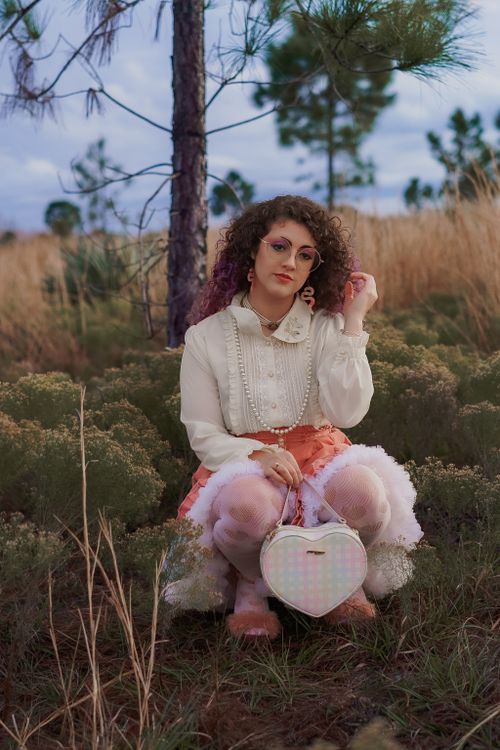 Free Woman with curly hair in a white blouse and pink skirt posing in a meadow. Stock Photo
