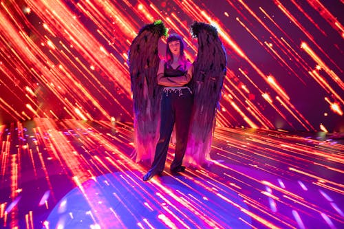 Woman with Dark Angel Wings Standing on Lit up Stage