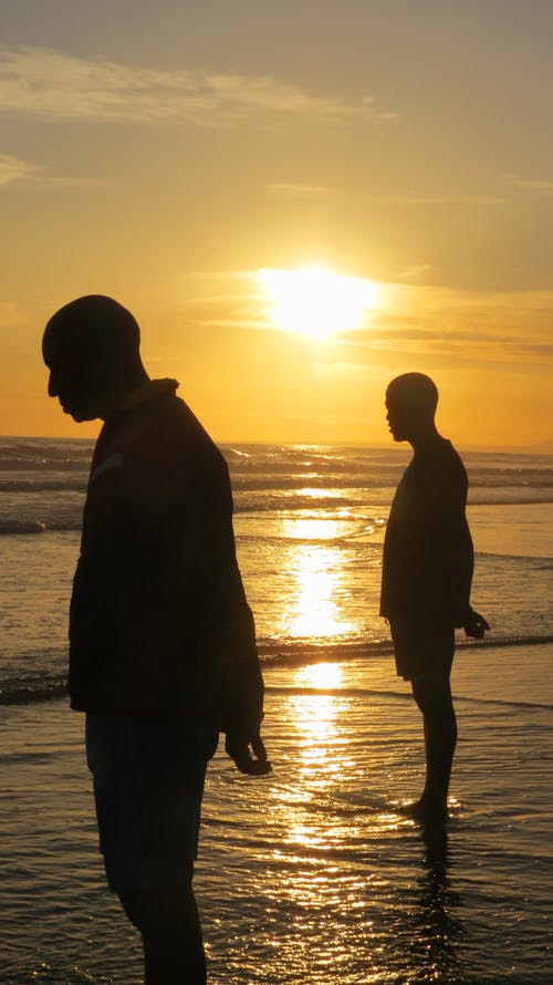 Two men walking on the beach at sunset