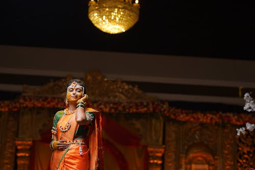 A woman in an orange sari is performing on stage