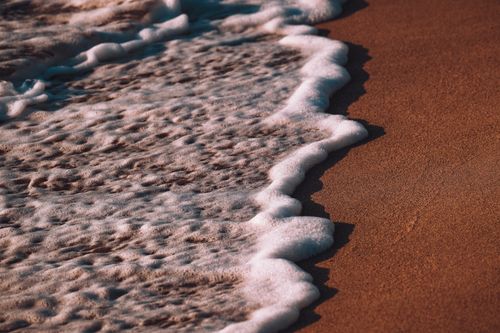 Free Close-up of gentle ocean waves washing over a sandy beach under warm sunlight. Stock Photo
