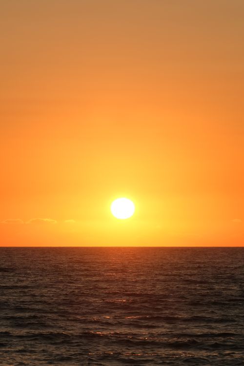 Free Captivating sunset over the ocean with vibrant orange and yellow hues lighting up the sky. Stock Photo
