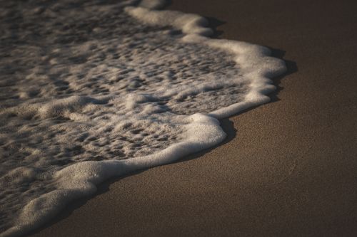 Free Tranquil ocean waves softly touching the sandy beach under the warm sunlight. Stock Photo