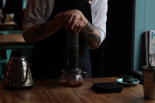 Barista making coffee using an Aeropress in a cozy café setting. Focus on hands and brewing process.