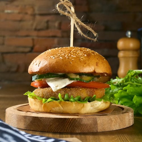 A burger with vegetables and cheese on a wooden cutting board