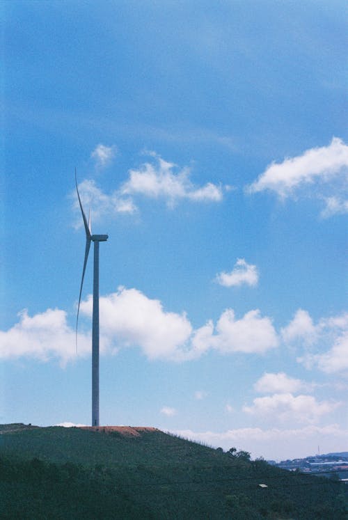 A wind turbine on a hill with blue sky