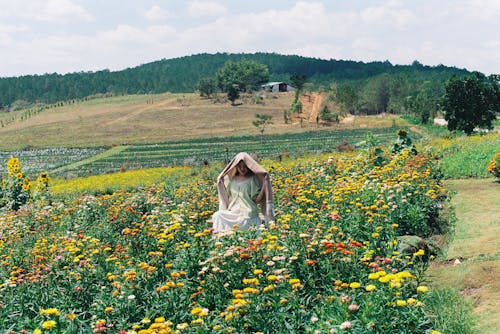 A woman in a white dress is walking through a field of flowers