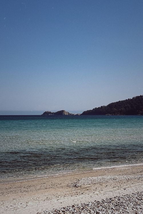 Free Peaceful Greek seaside view with clear blue waters and a distant rocky coastline. Stock Photo