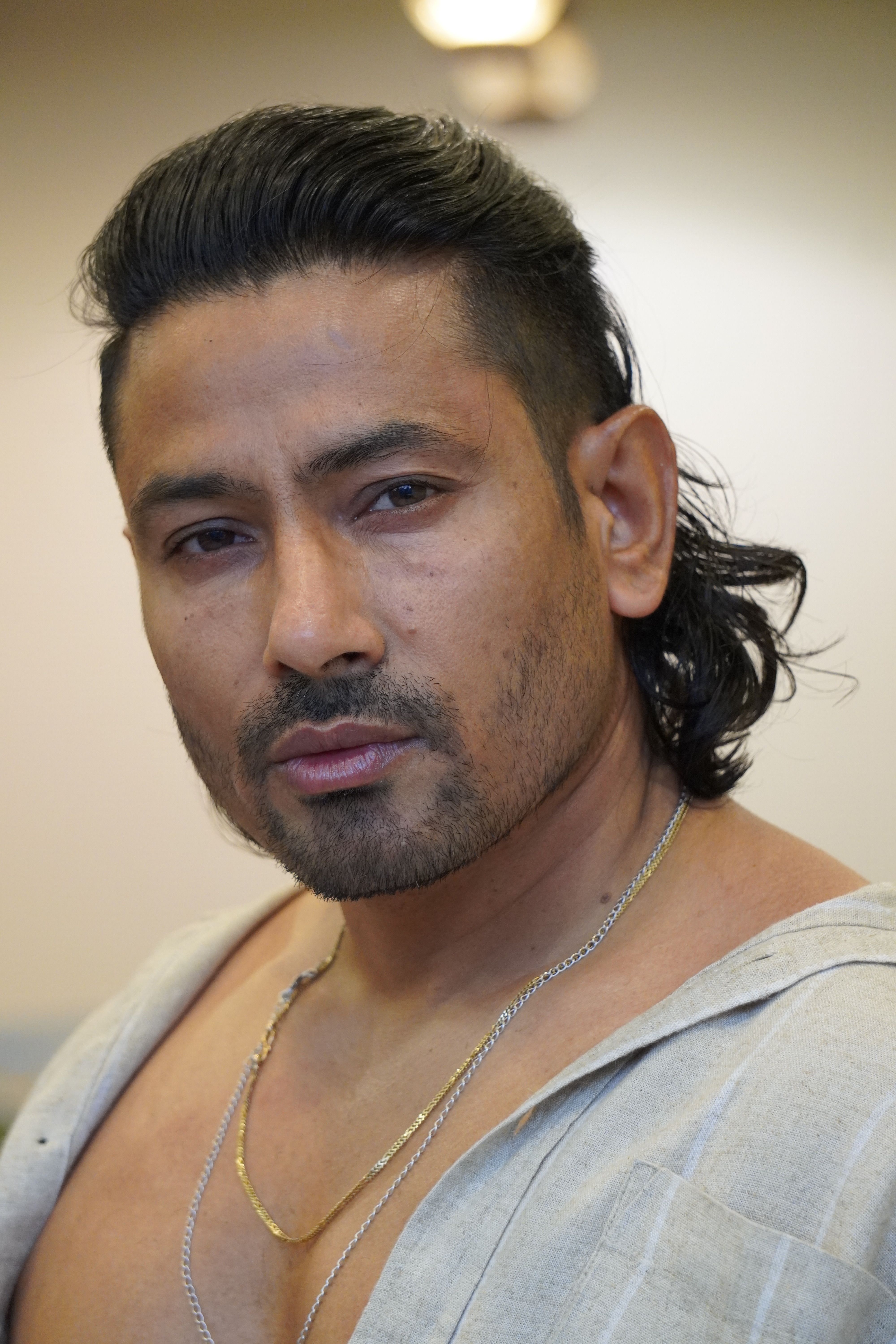 Close-up portrait of a man with a necklace, wearing a light shirt.