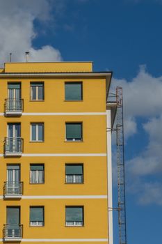 A modern yellow apartment building with balconies and a clear blue sky.