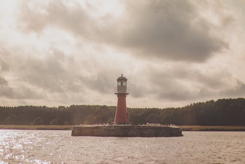 A lighthouse is on a body of water with clouds